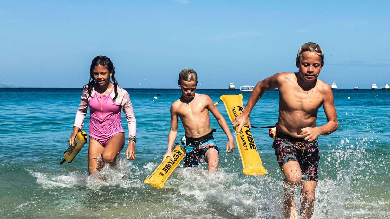 Three children running through shallow water at the beach holding yellow RESTUBE swim buoys