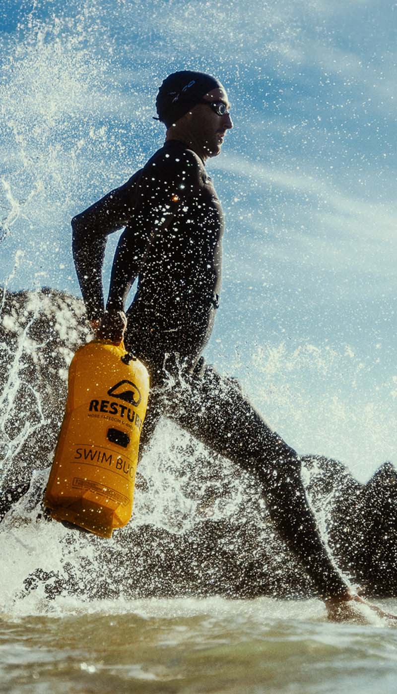 Athlete in wetsuit running from the water with RESTUBE Swim Buoy – a dynamic scene full of energy and safety.