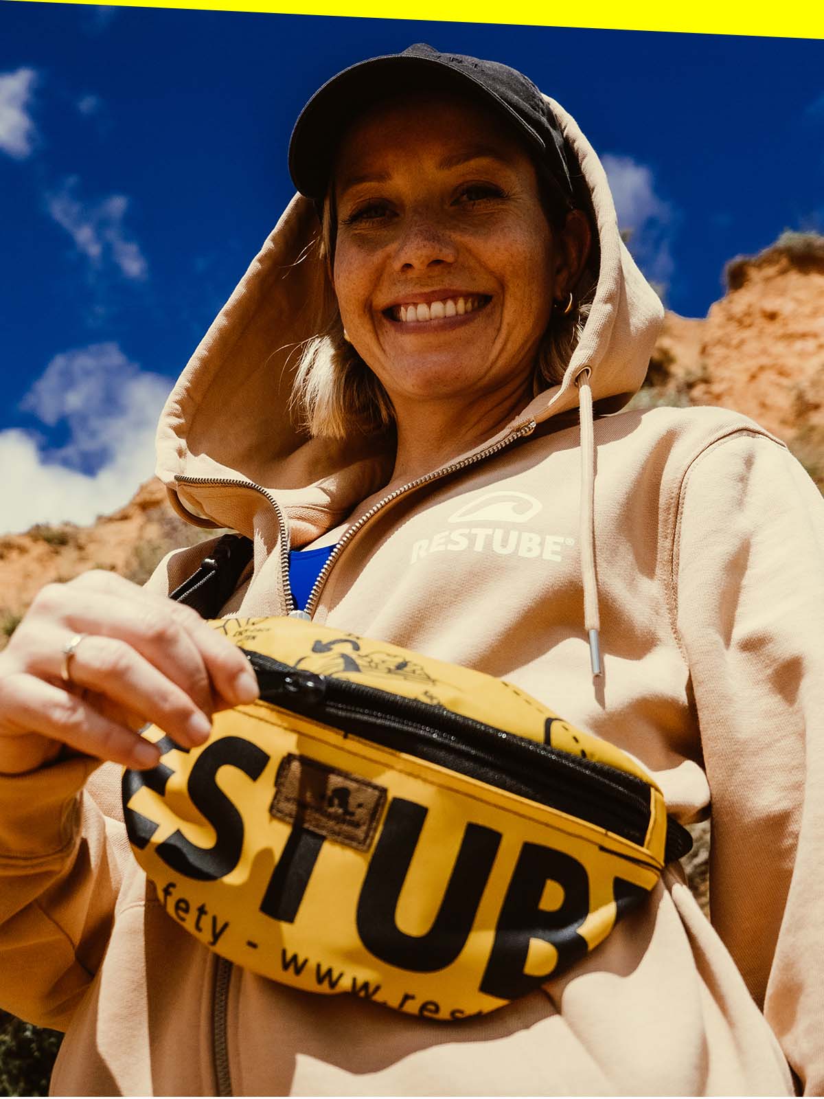 A happy woman with RESTUBE waist pouch wearing a RESTUBE zip-up hoodie in an outdoor environment.
