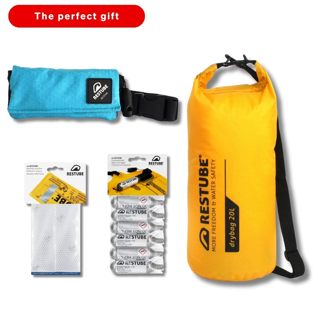 A Restube gift bundle including a yellow 20L dry bag, a turquoise Restube Active pouch, CO₂ cartridges, a rearming kit, and reflective patches, presented with the label “The perfect gift.”*