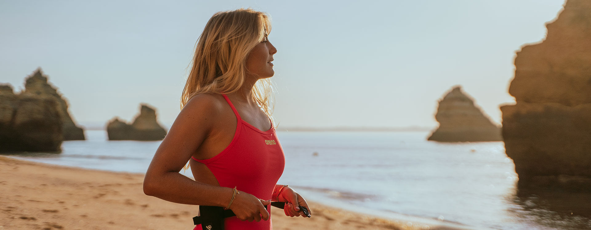 A woman in a red swim suit on the beach , strapping the RESTUBE safety buoy to her waist – ready for water activity.