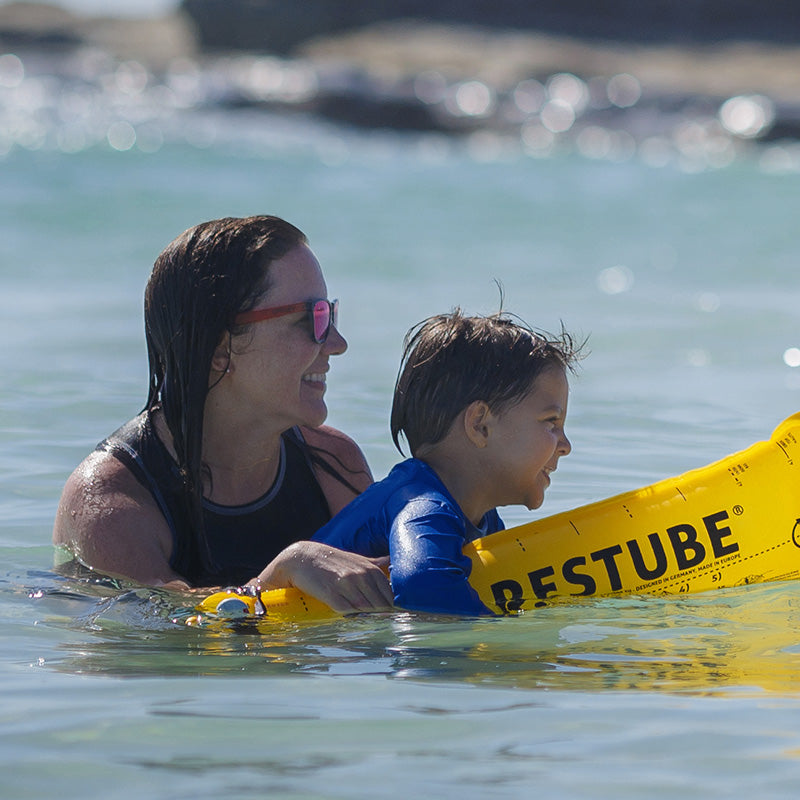 An adult and child with yellow RESTUBE safety buoy in the water – smiling and safe.