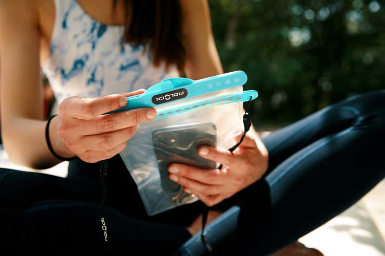 A woman in a sporty outfit sitting outdoors, examining the waterproof pouch in her hands.
