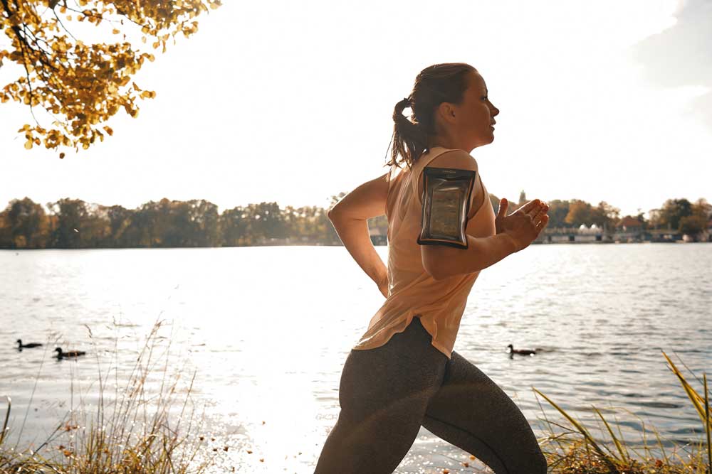 Runner with waterproof phone case by the lake in sunlight.