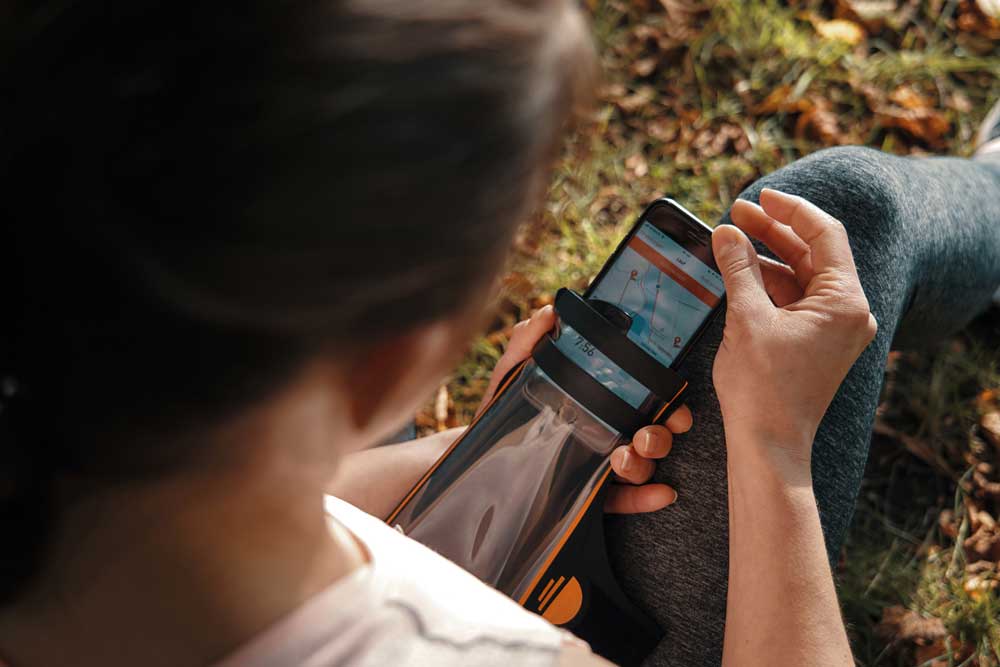 Waterproof phone case in use during outdoor adventure - a woman sits on the grass, opening the case and looking at the maps on her phone.