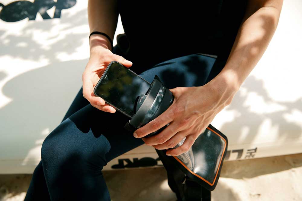 Waterproof phone case by RESTUBE in use at the beach - a person sitting on a SUP board, taking the phone out of its case.