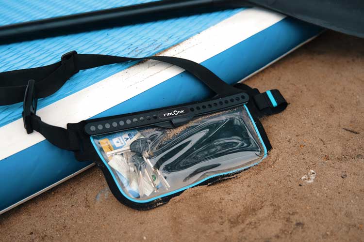 Waterproof waist pouch with viewing window placed on a SUP board at the beach.