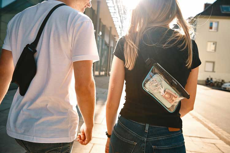 Fidlock Hermetic waterproof slingbags being worn during a sunny walk by a woman and a man.