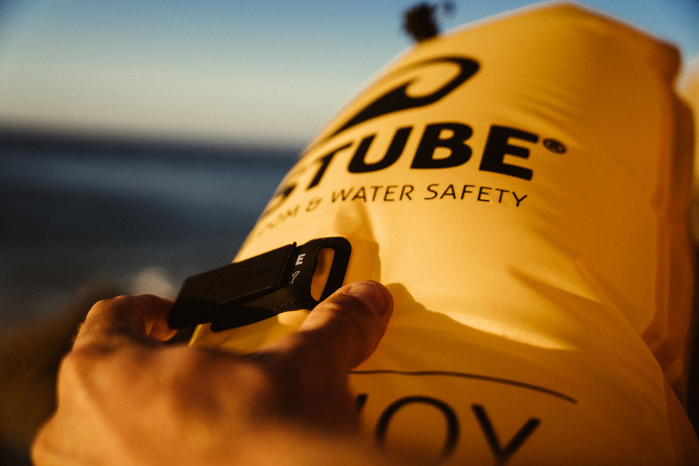 Inflatable RESTUBE swim buoy on the beach at sunset, a person adjusting an add-on onto it.