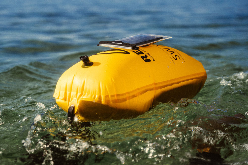 Yellow RESTUBE swim buoy with a water-resistent phone case floating on top of the water.