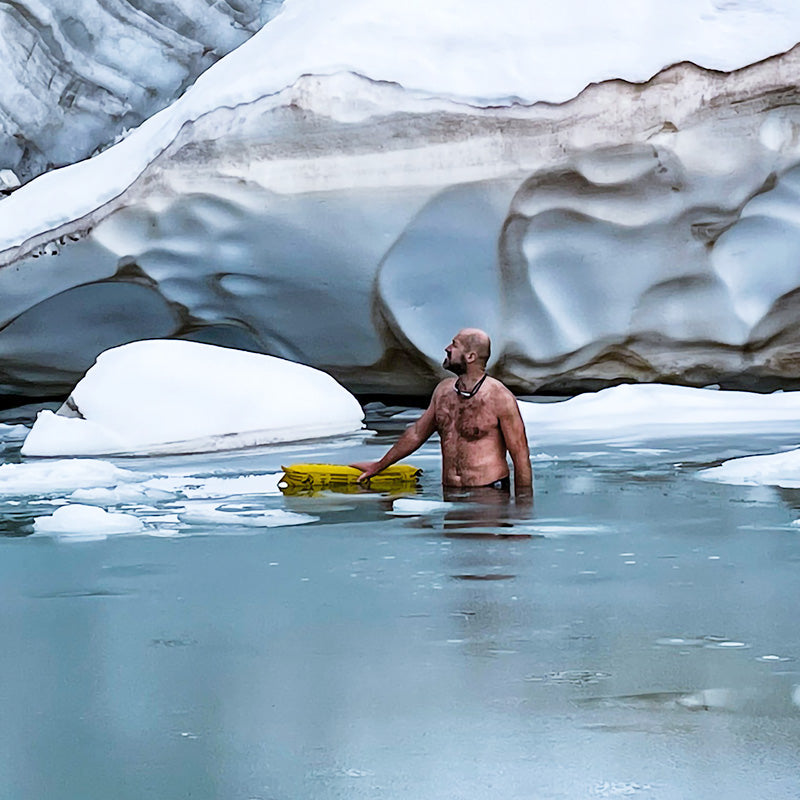 Man with yellow RESTUBE buoy in icy water in front of a glacier backdrop.