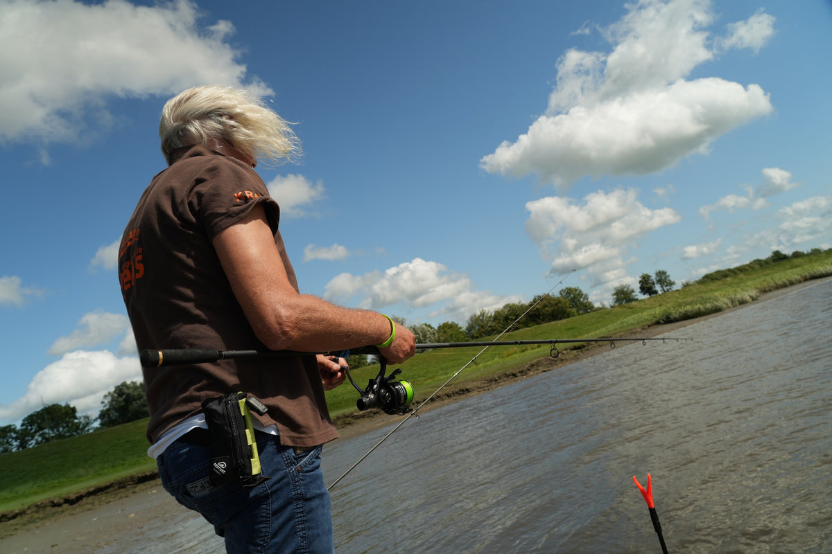 Jörg Ovens casting from a riverbank under a blue sky, with the RESTUBE EXTREME attached to his belt