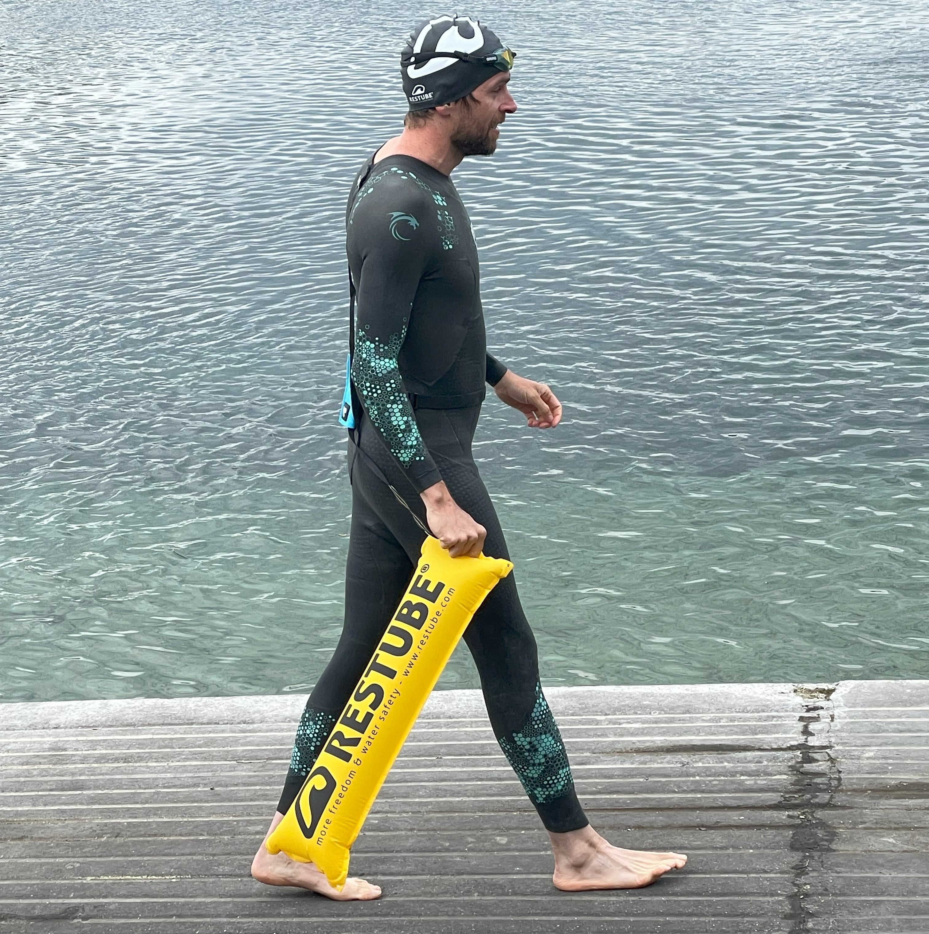 An athlete with a yellow RESTUBE safety buoy at the lake shore on a pier.