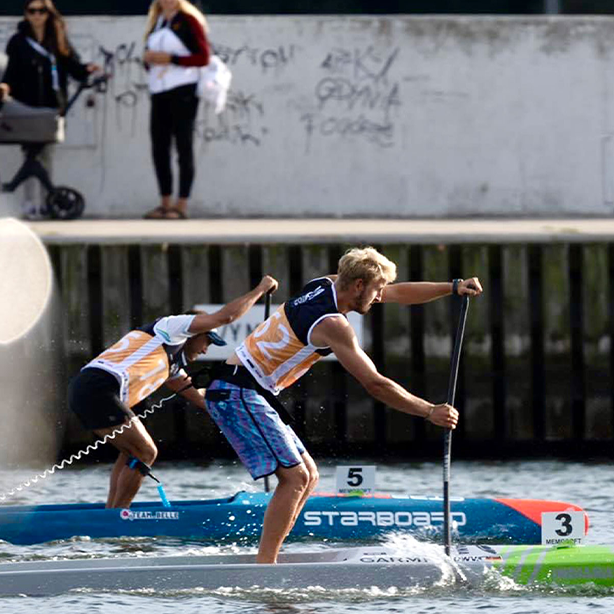 Two SUP competitors paddling powerfully side by side, each wearing RESTUBE – visible protection during intense action.