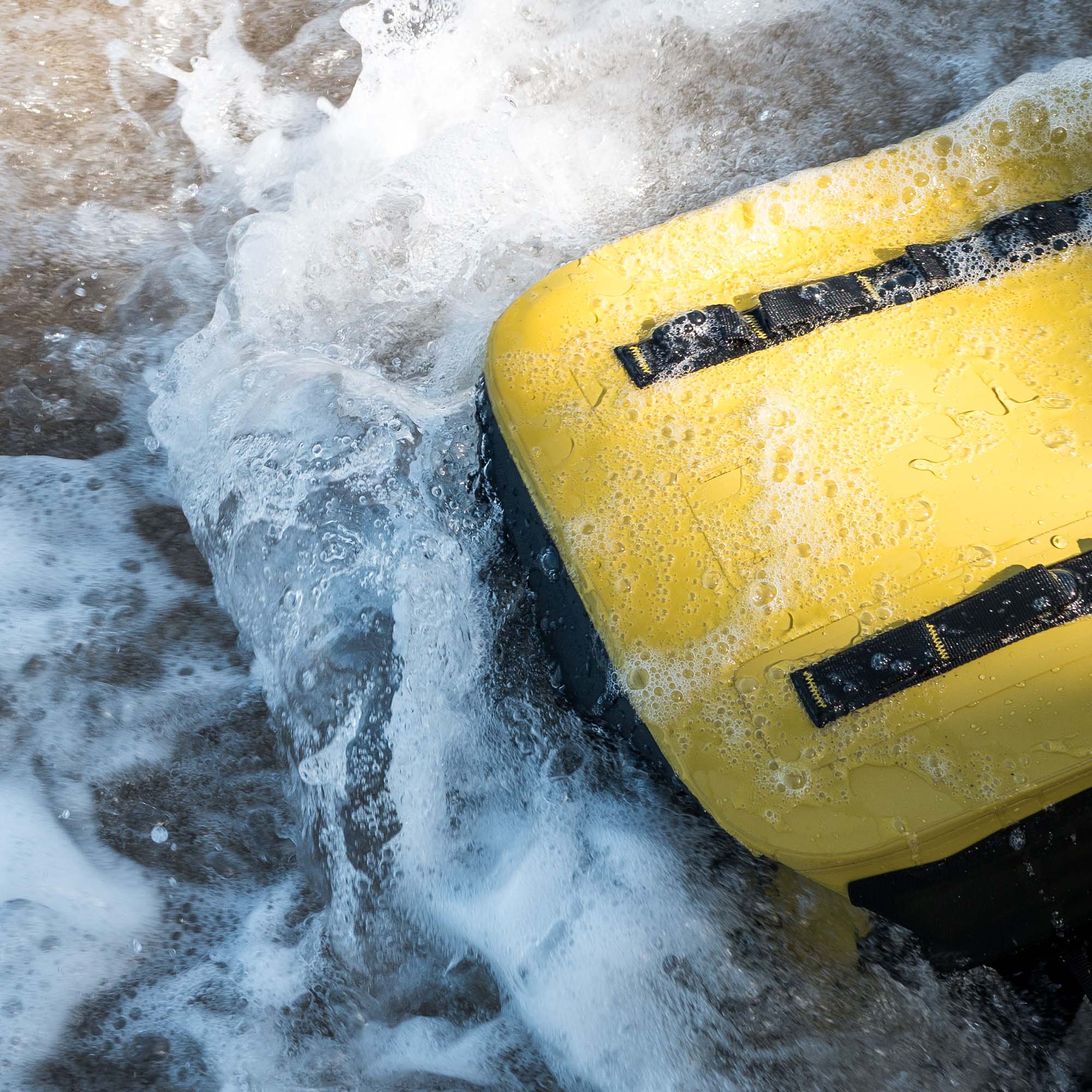 Yellow RESTUBE backpack base in shallow water with waves splashing, showcasing water resistance and rugged construction