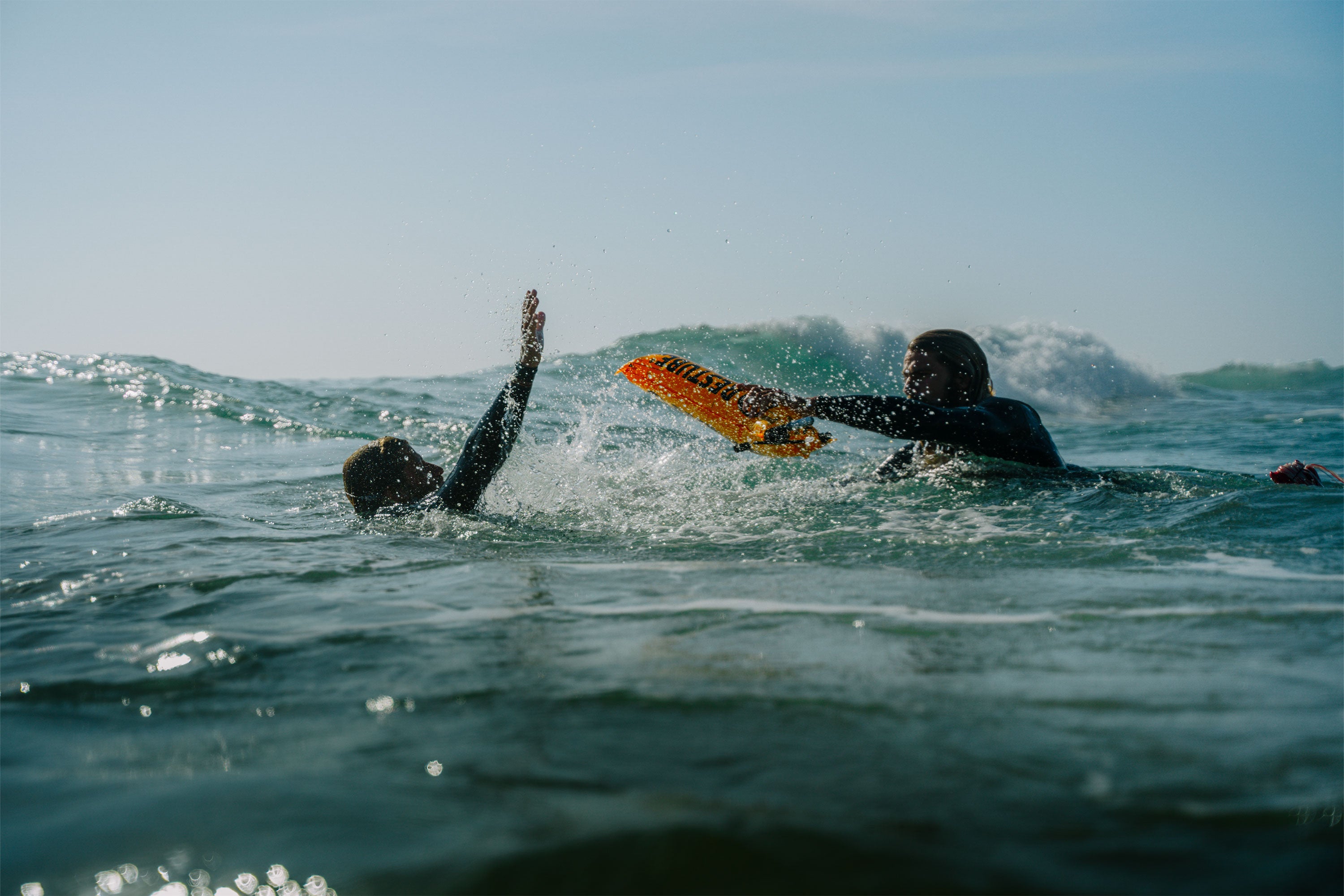 Ocean rescue scene: One person extends a bright orange RESTUBE rescue buoy to another in distress – bringing buoyancy and safety in rough waters.