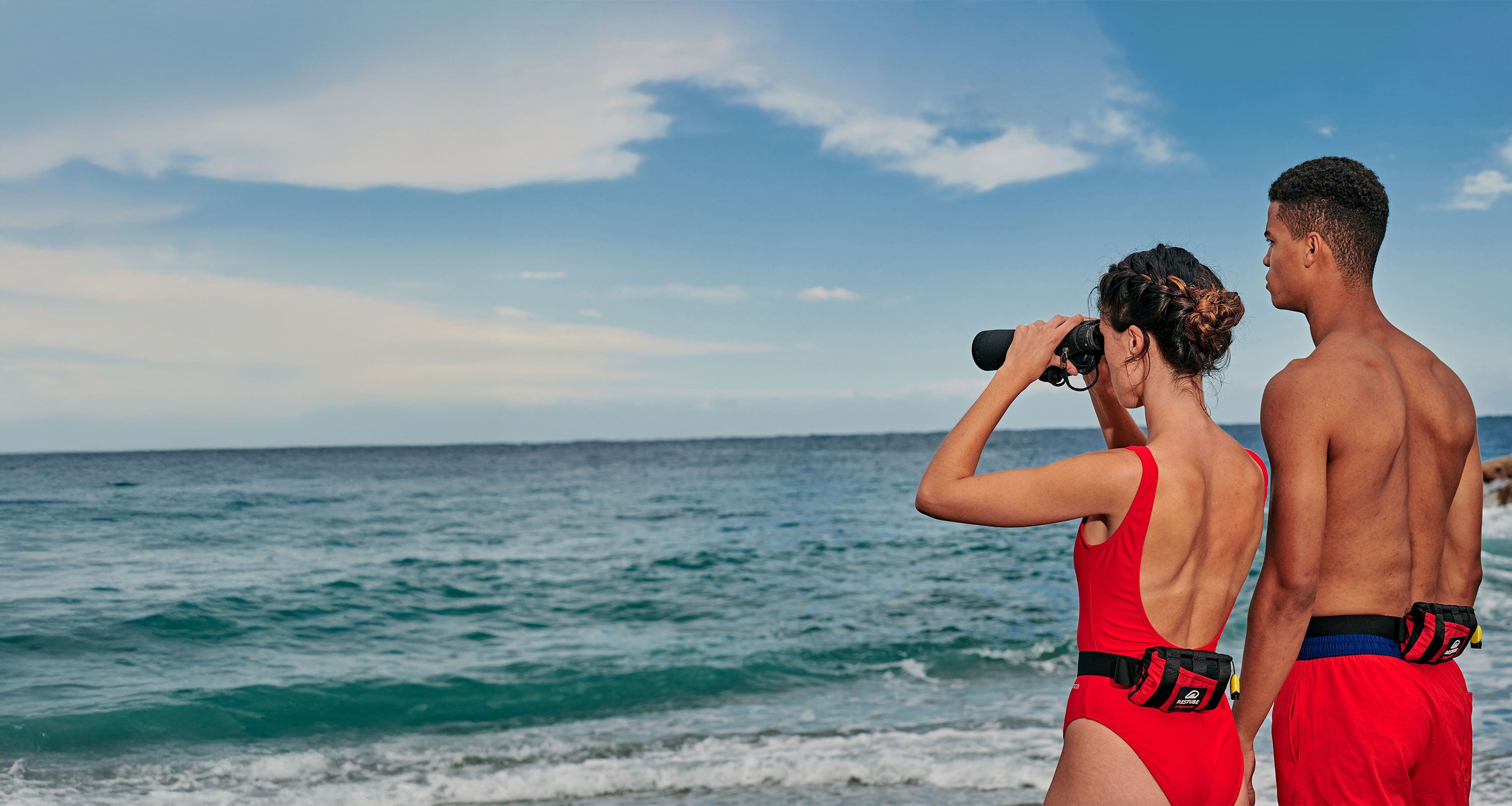 Two lifeguards with RESTUBE buoy on the beach – one looking through binoculars.