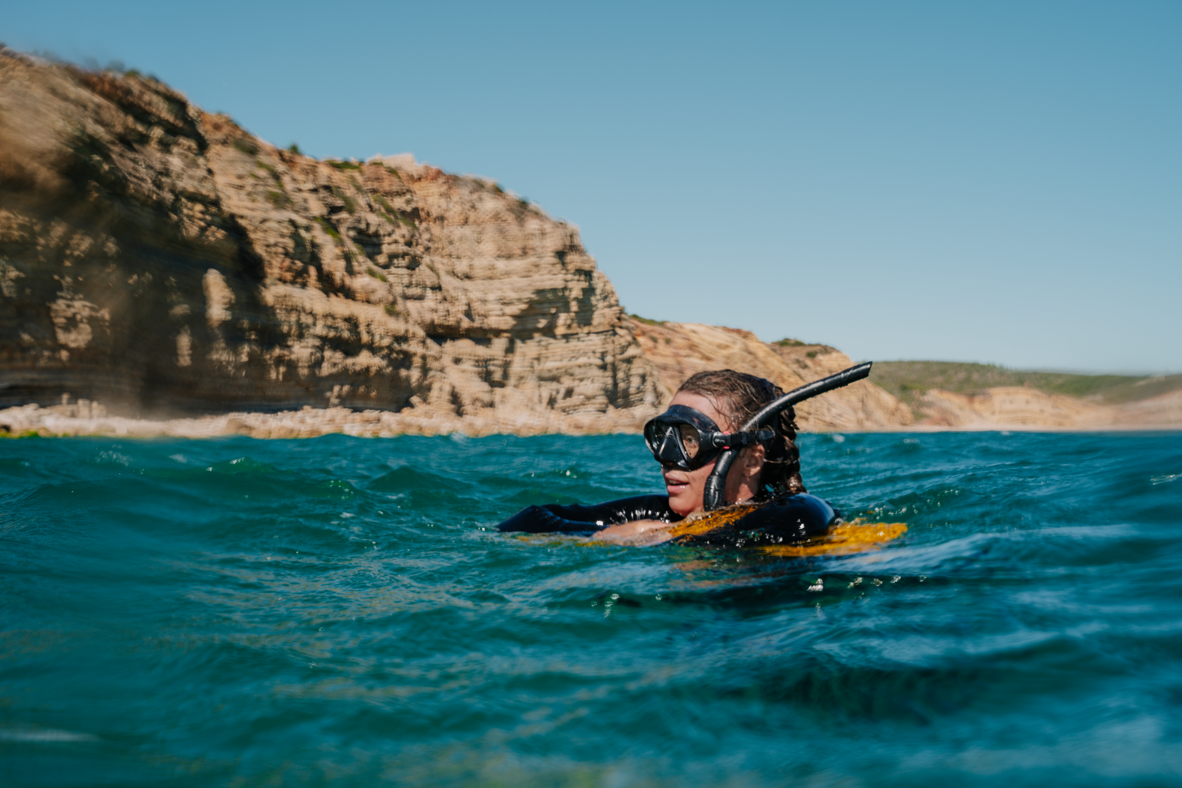 Snorkeler with RESTUBE buoy in the sea near rocky coast – for water safety.