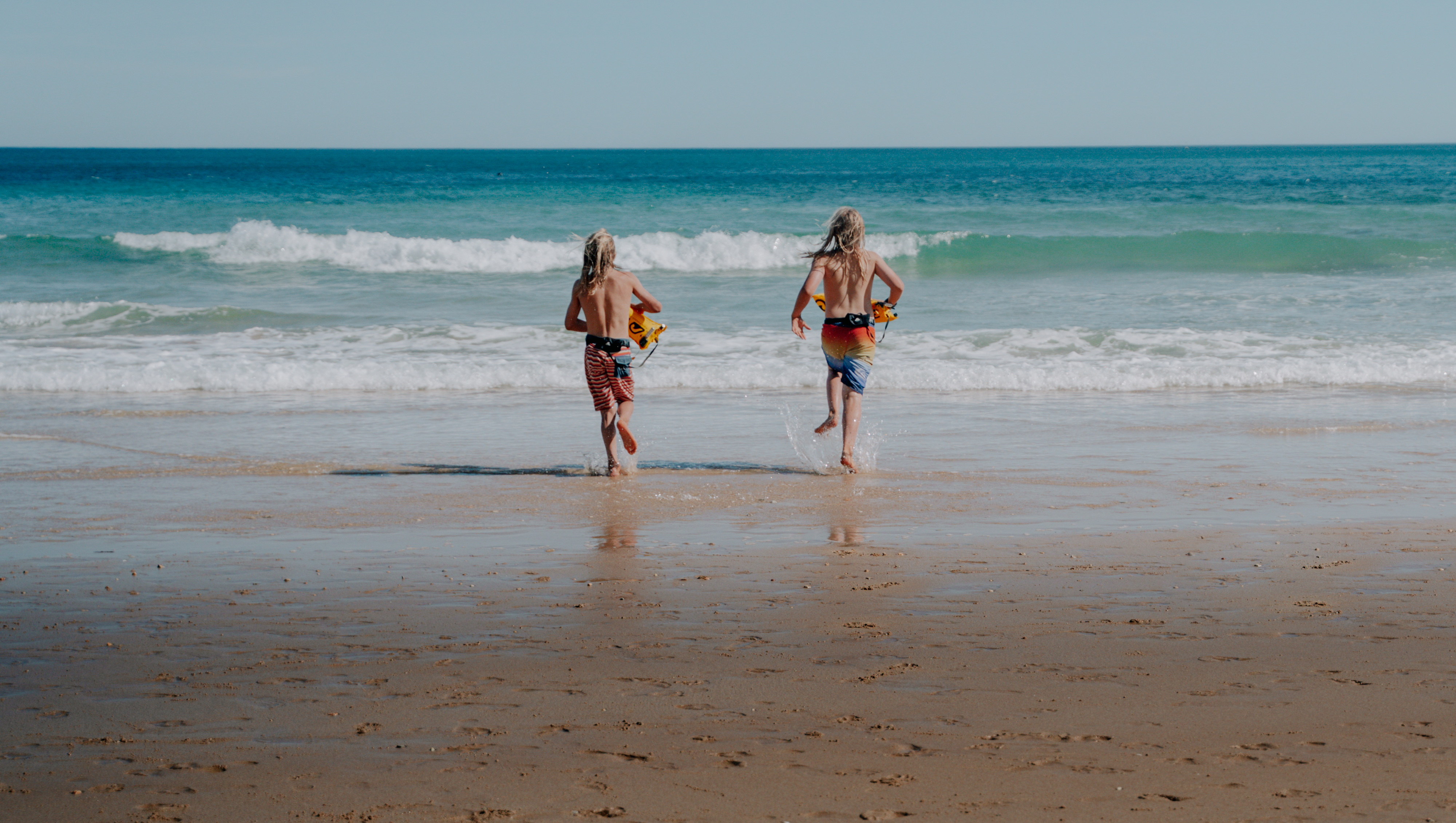 Two children with RESTUBE safety buoys running into the sea from the beach.