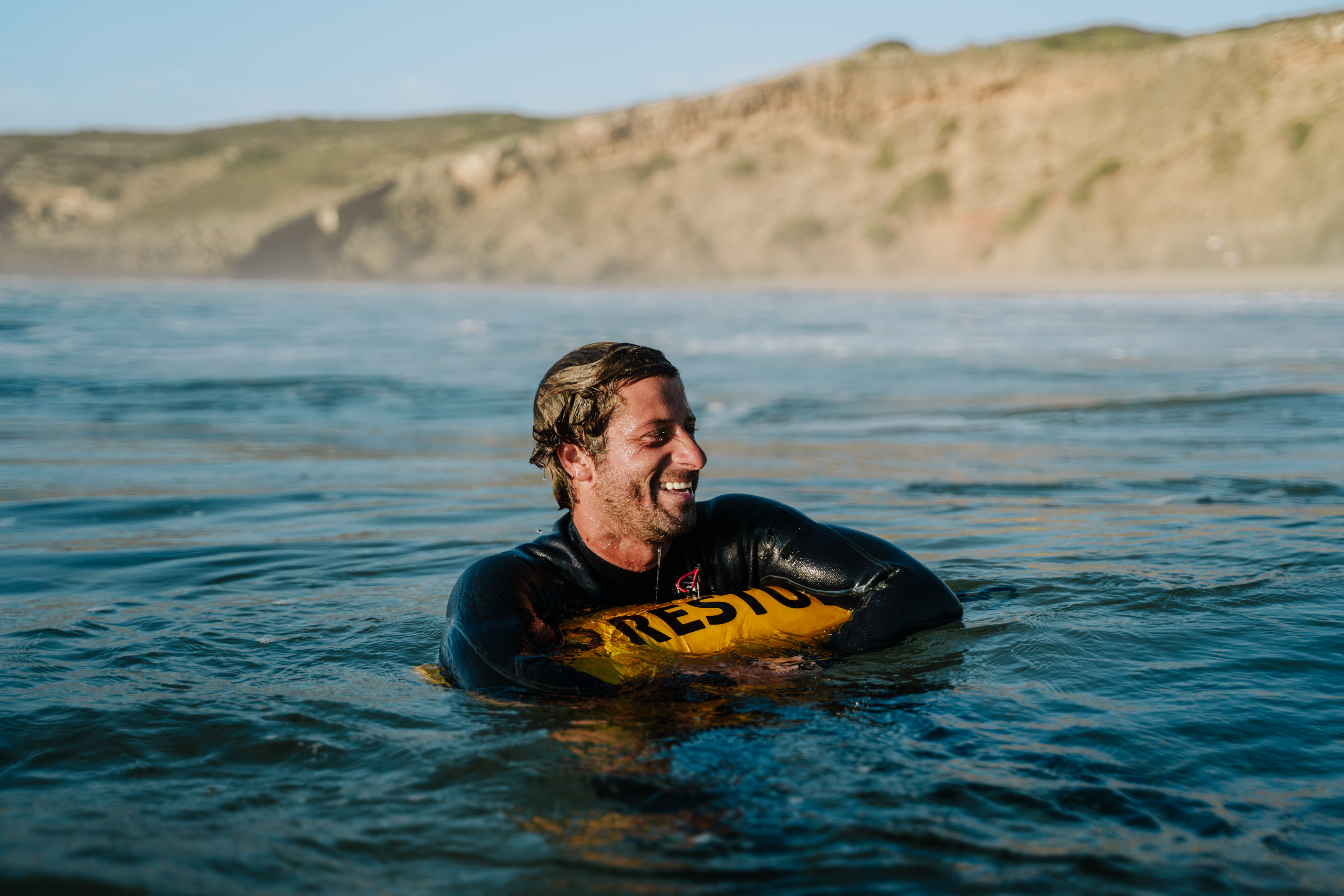 Smiling man in a wetsuit holding onto his RESTUBE buoy – relaxed safety while swimming in open water.
