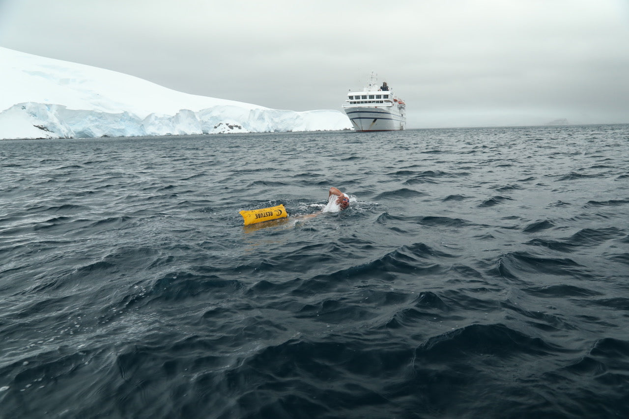 A swimmer with yellow RESTUBE buoy in icy water in front of a cruise ship.