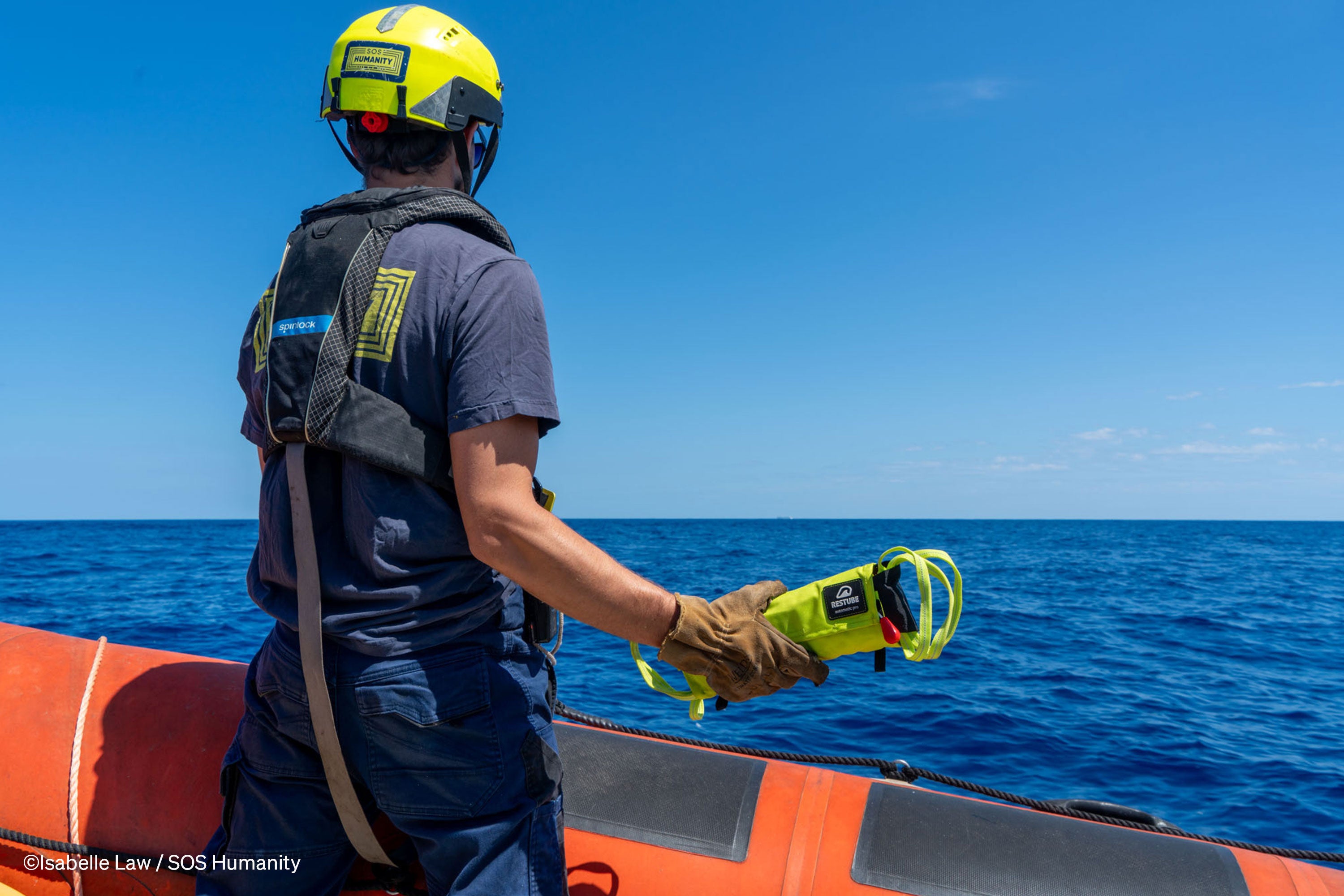 Rescue worker on a boat holding a RESTUBE AUTOMATIC 180 emergency flotation device, ready for water rescue operations at sea.