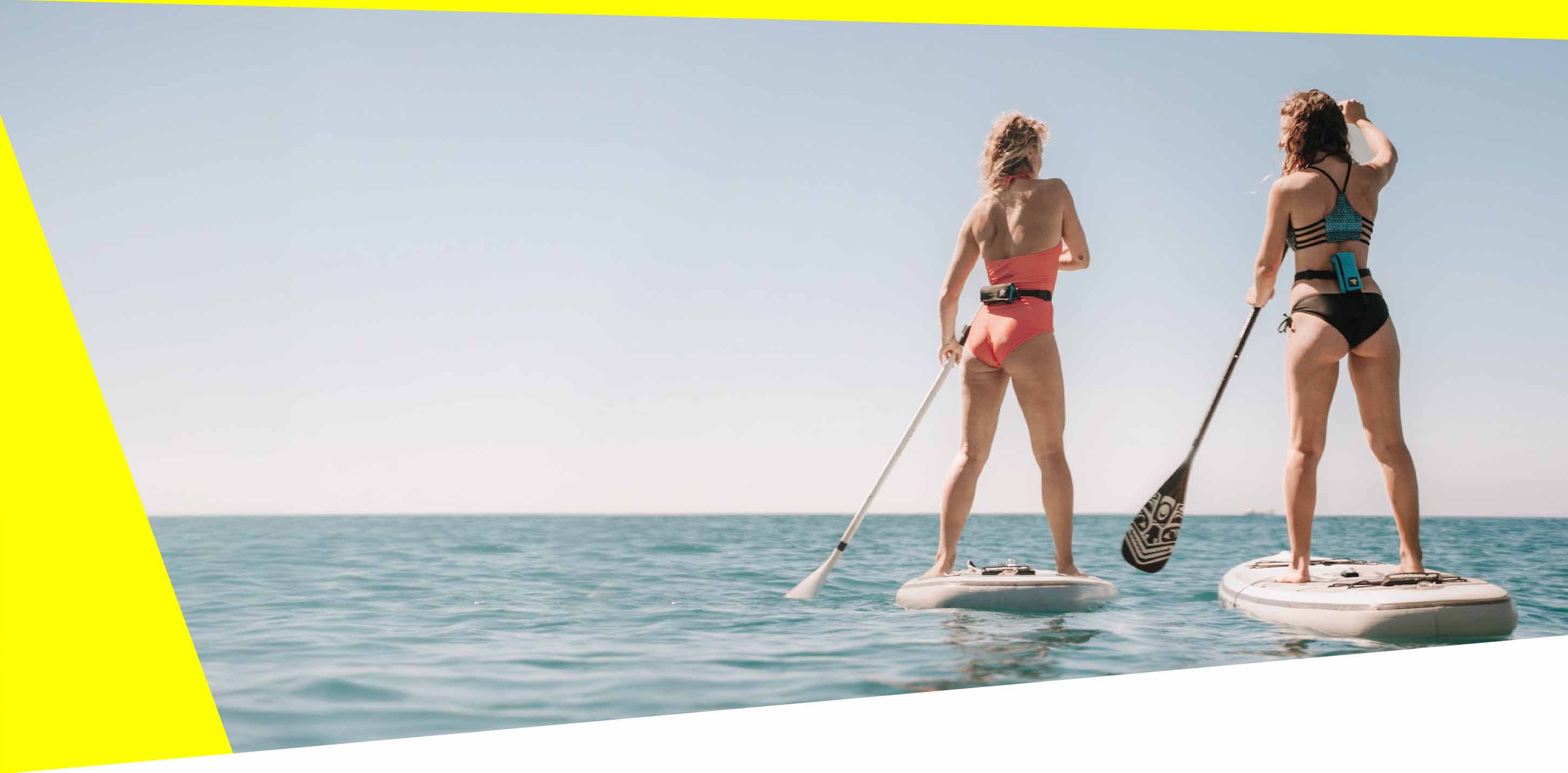 Two women with RESTUBE buoy stand-up paddling on the open sea.