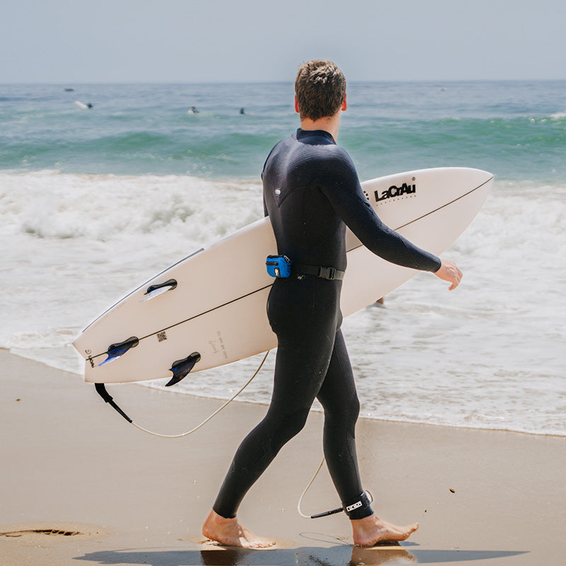 Surfer with RESTUBE buoy on belt walks into the water from the beach.