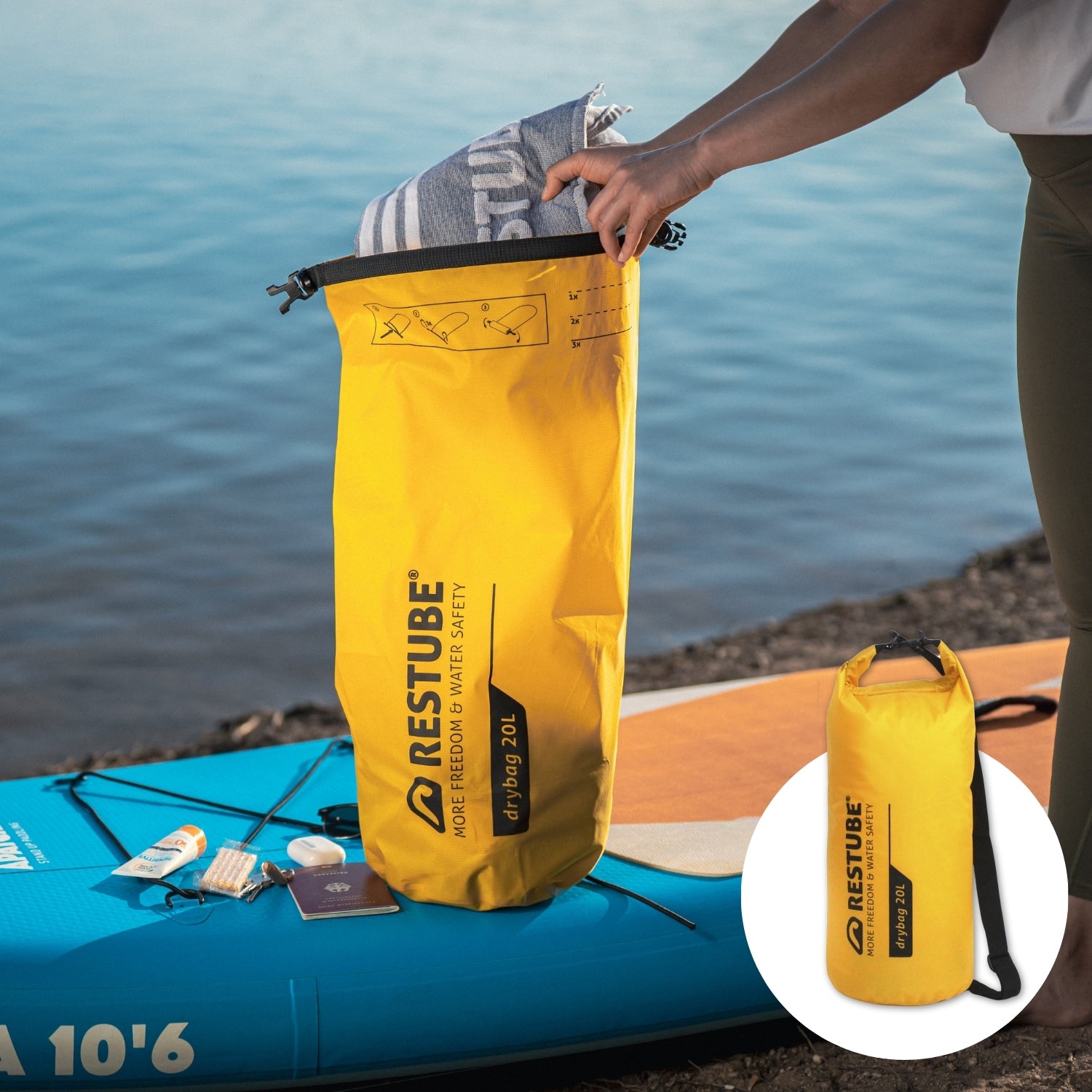 Waterproof yellow RESTUBE 20 Liter Drybag on the SUP Board by the lake together with a suncream, a passport, headphones - a person putting the RESTUBE towel inside