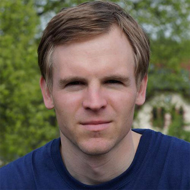 A portrait of young man (Wolfgang Grohe) with short light brown hair, neutral expression, blue shirt – soft green outdoor background, calm and focused.