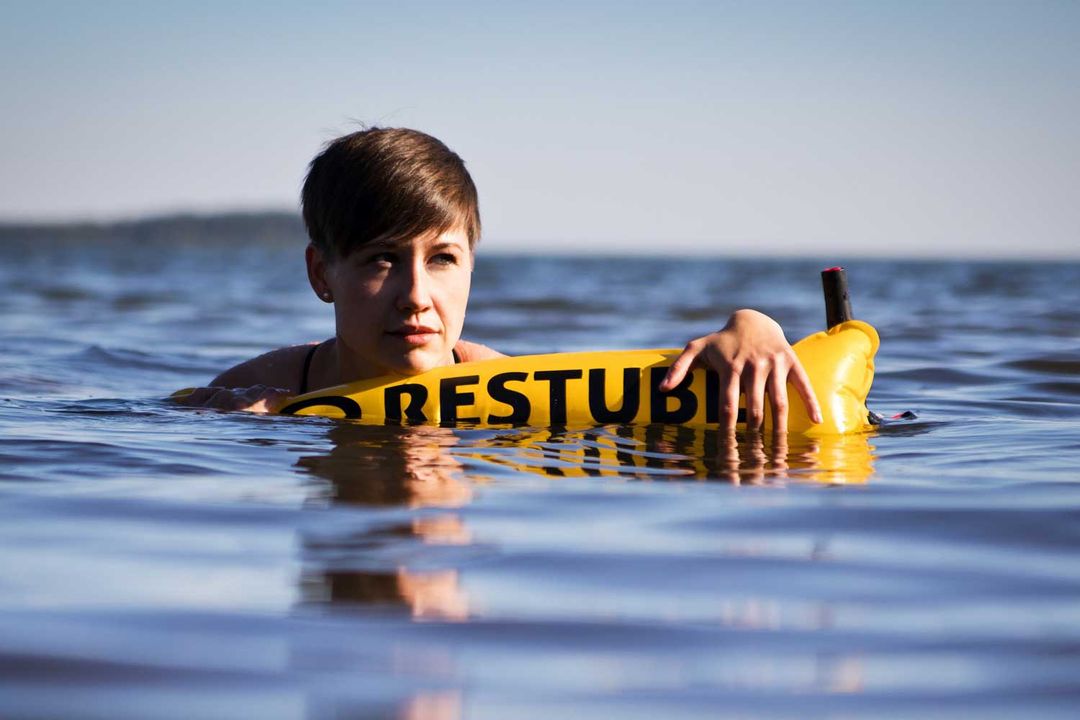 A person with short hair in the water with yellow RESTUBE safety buoy – for flotation and visibility.