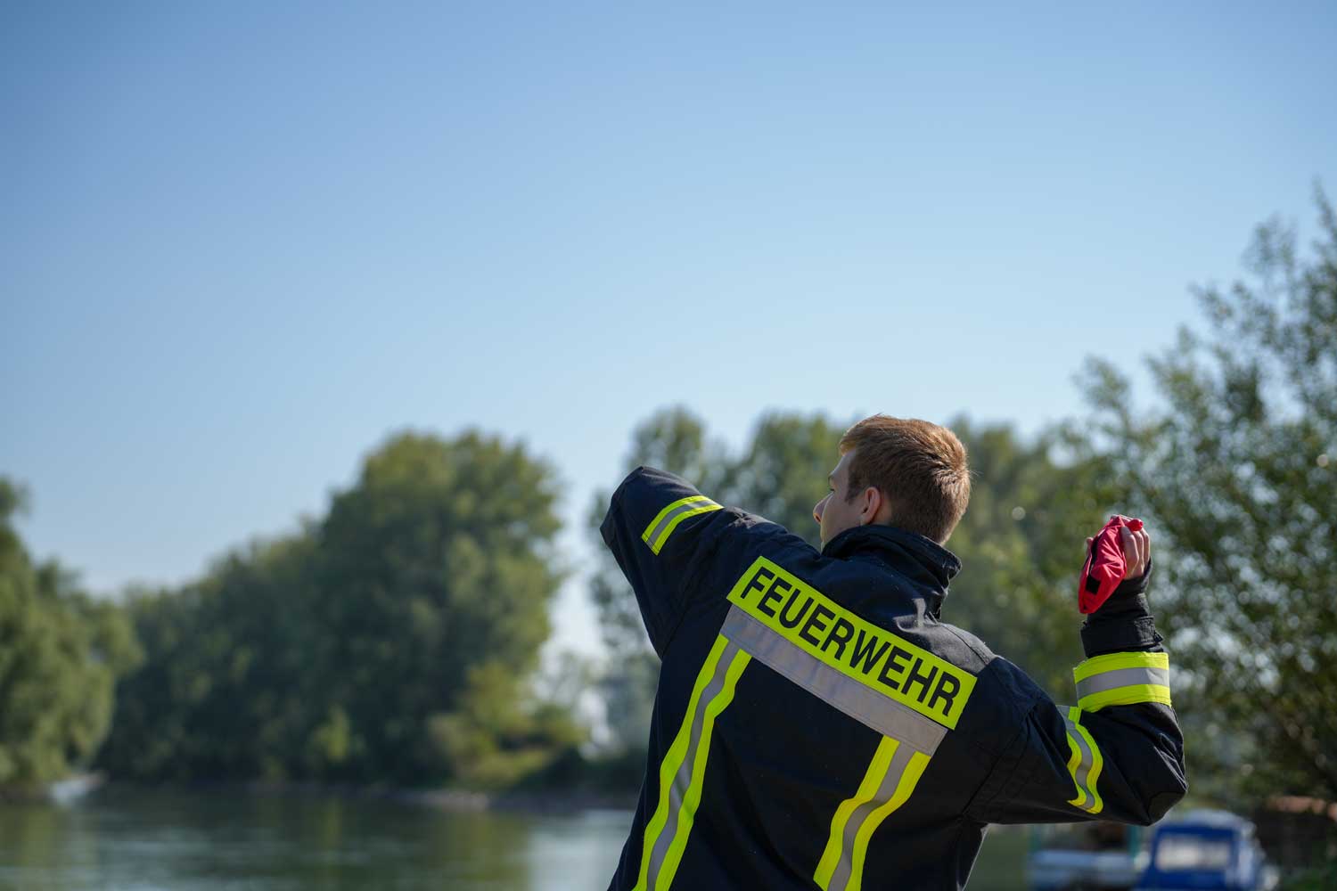A german firefighter throwing a rescue buoy by the river, a word "FEUERWEHR" on the back of his dark-blue jacket