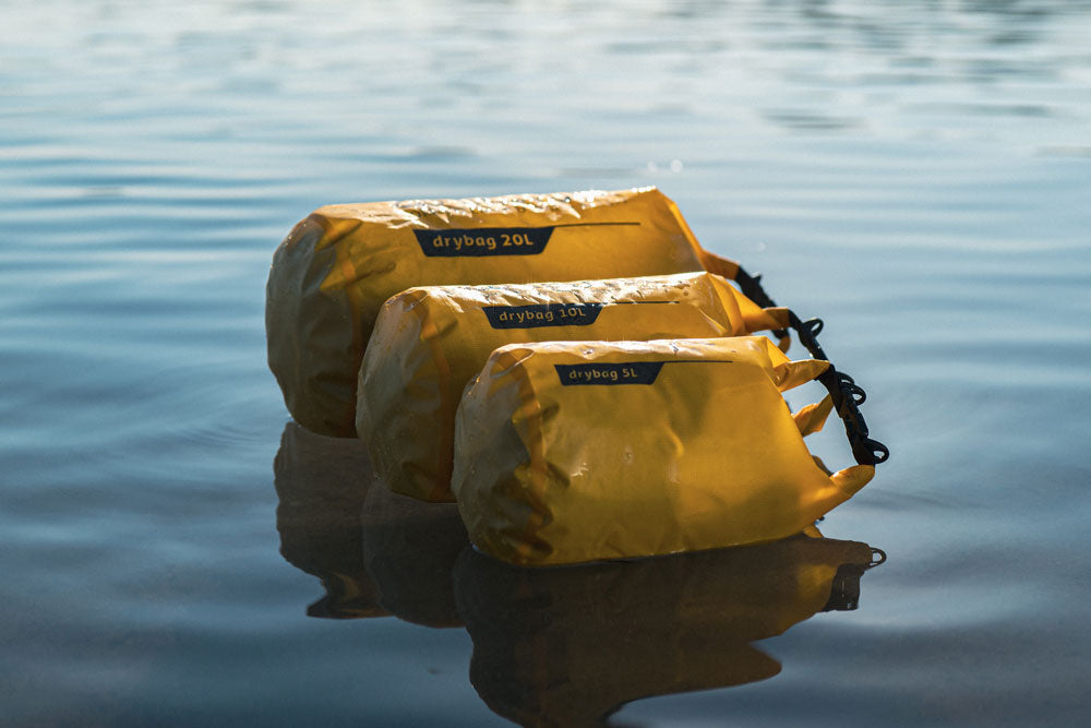 Yellow RESTUBE Drybags in various sizes ( 5 L, 10 L and 30 L) floating on calm water.