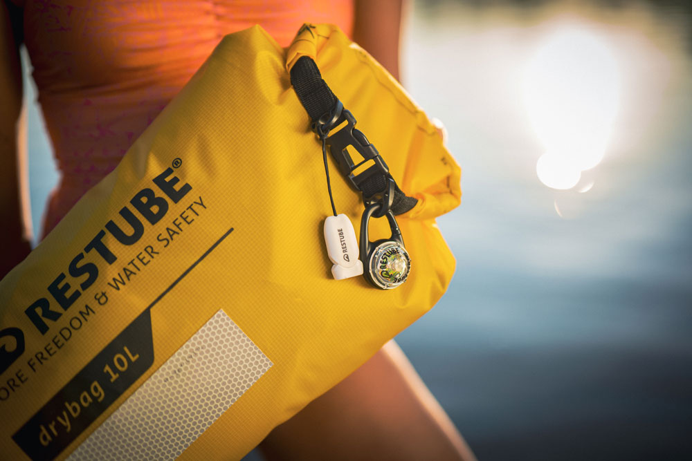 A close-up shot of a person holding a yellow RESTUBE Drybag 10L with useful add-ons - an LED light and a whistle.