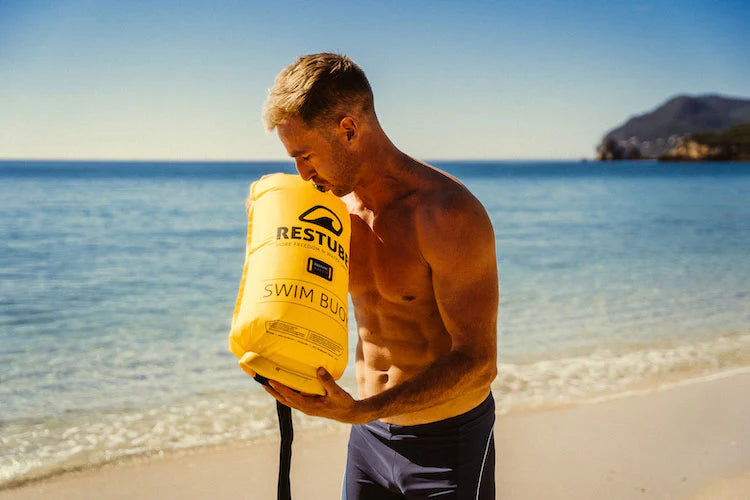 Man on the beach blowing yellow RESTUBE swim buoy – prepared for the water.