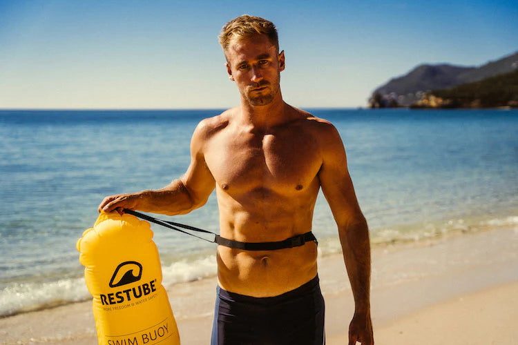Man on the beach with yellow RESTUBE swim buoy for watersports.