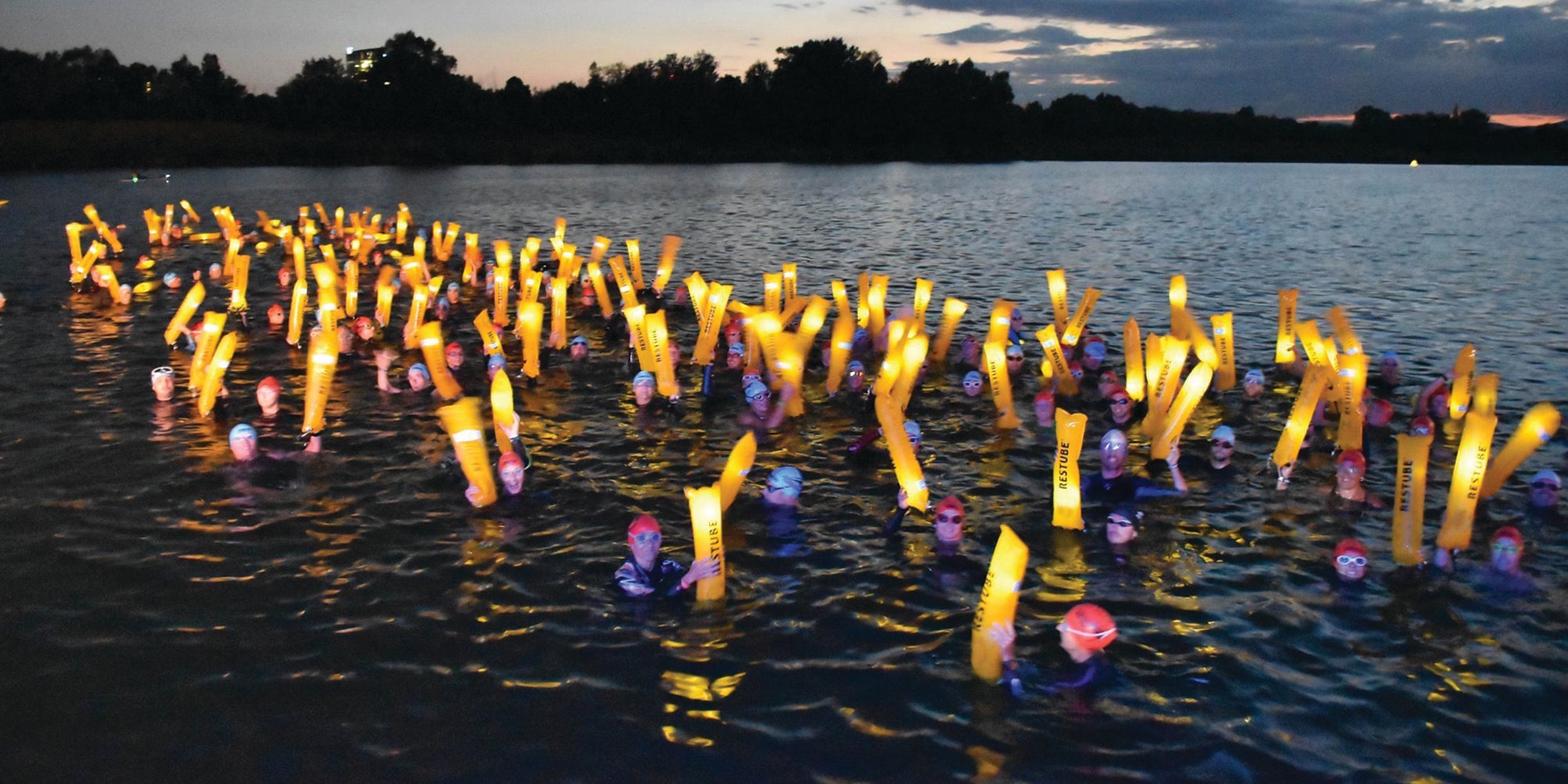 Dozens of swimmers at dusk with glowing RESTUBE buoys – high visibility, shared moments, and maximum safety.