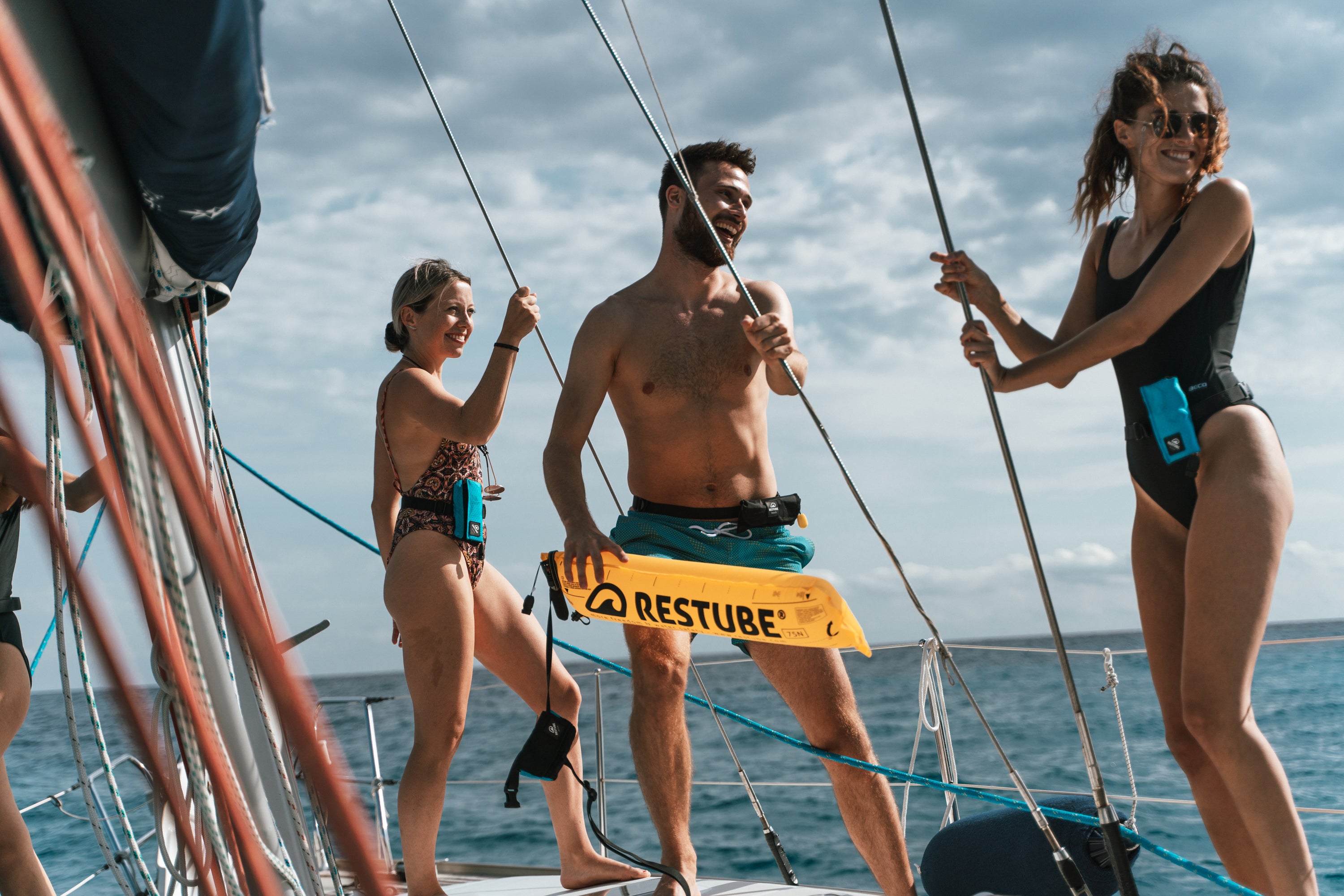 Three people on a sailboat with RESTUBE safety buoys, smiling and ready for watersports.