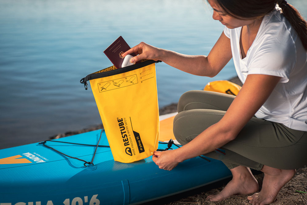 A woman packing the waterproof RESTUBE 5 Liter Drybag by the lake onthe paddleboard – ideal for safe storage during watersports.