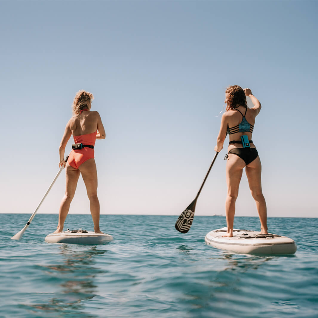 Two women with RESTUBE buoys stand-up paddling on the open sea.