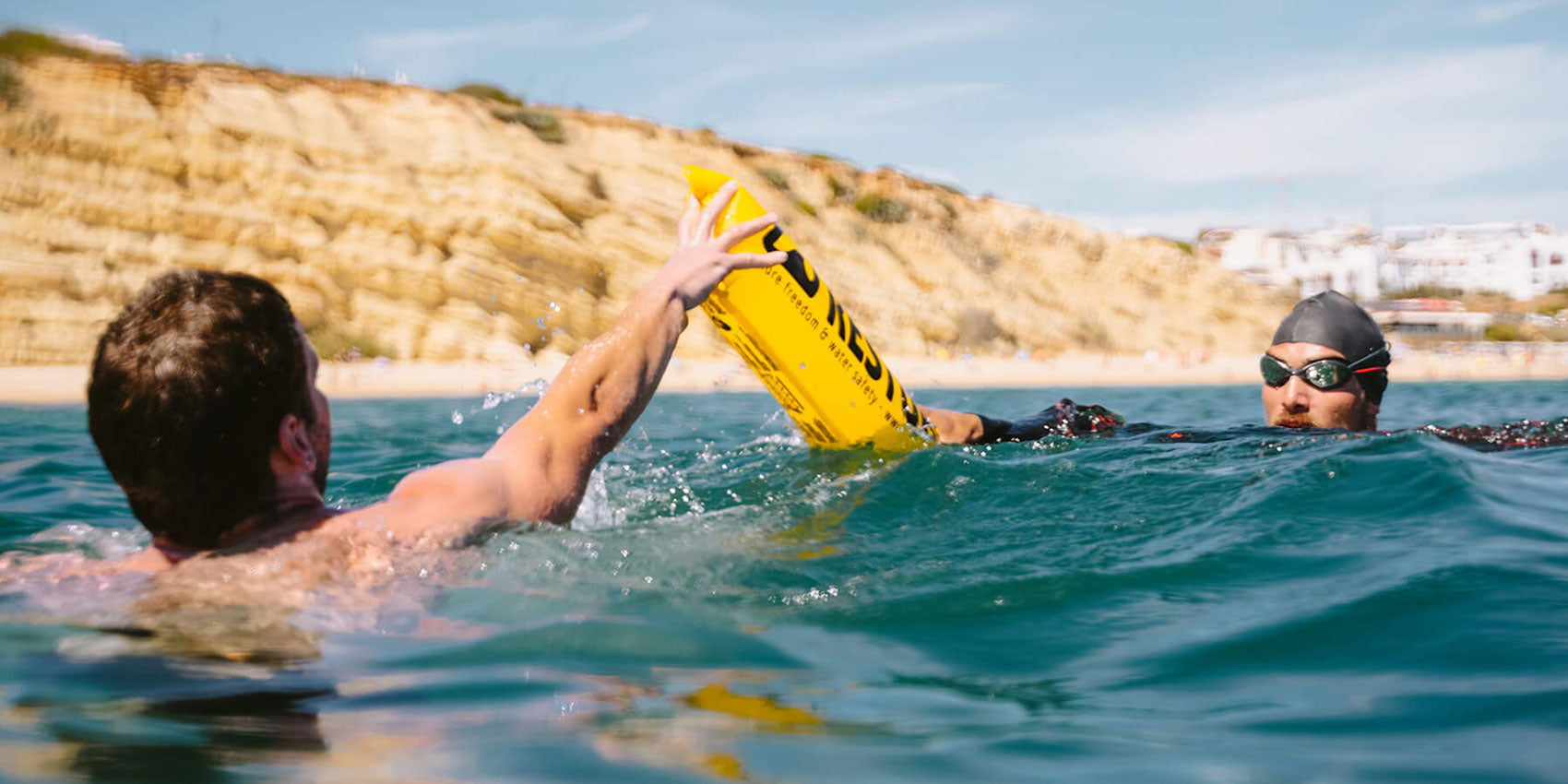 A swimmer with RESTUBE buoy in a rescue situation near rocky coast, handing the safety buoy to another swimmer