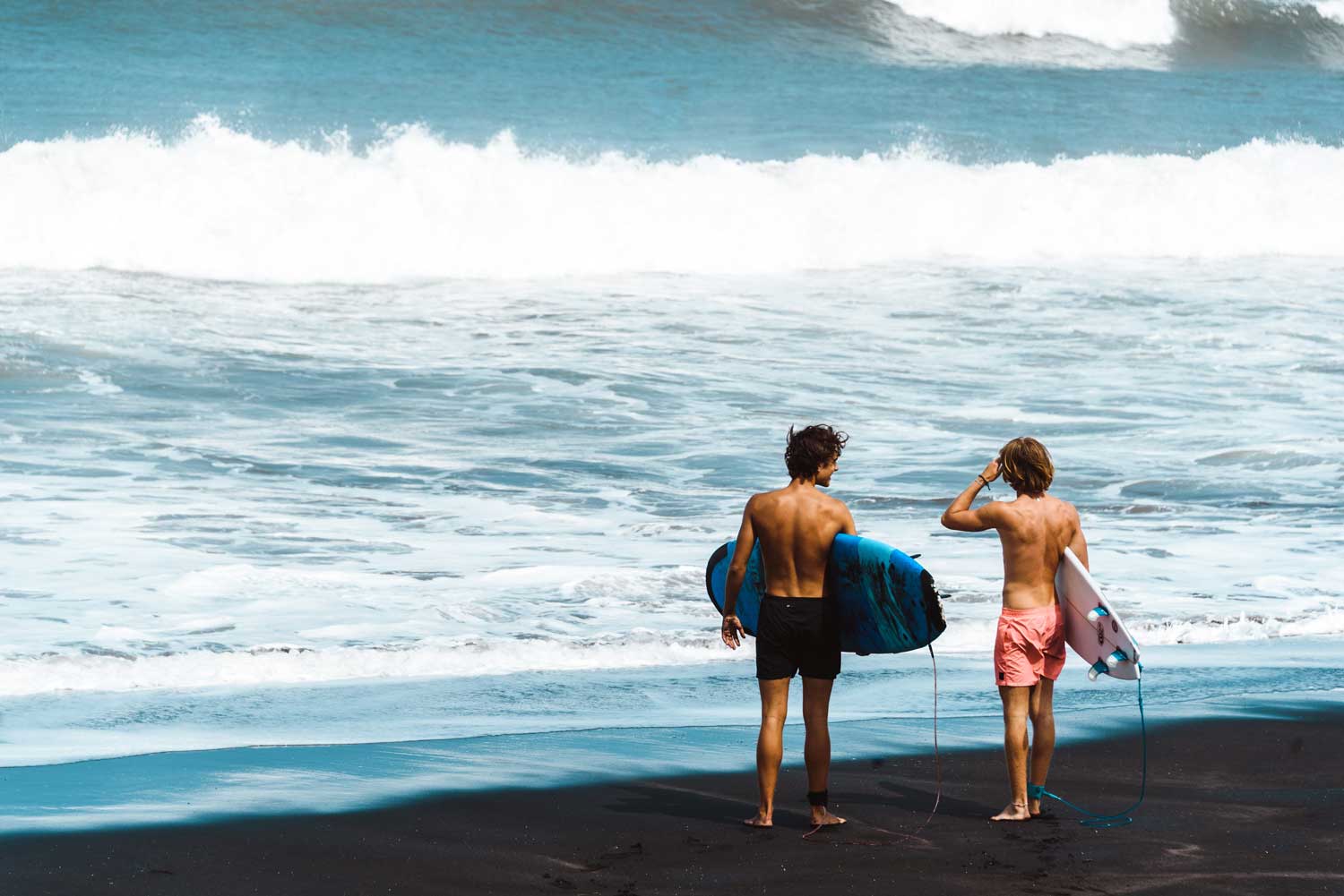 Surfer stehen am Strand und schauen auf die Wellen des Meeres