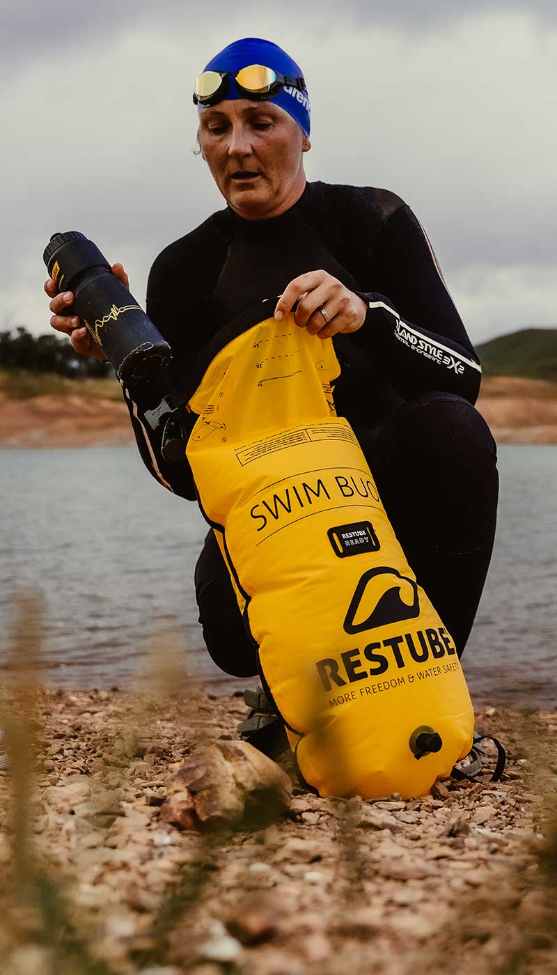 Swimmer at the lake’s edge with yellow RESTUBE swim buoy – ready for watersports.