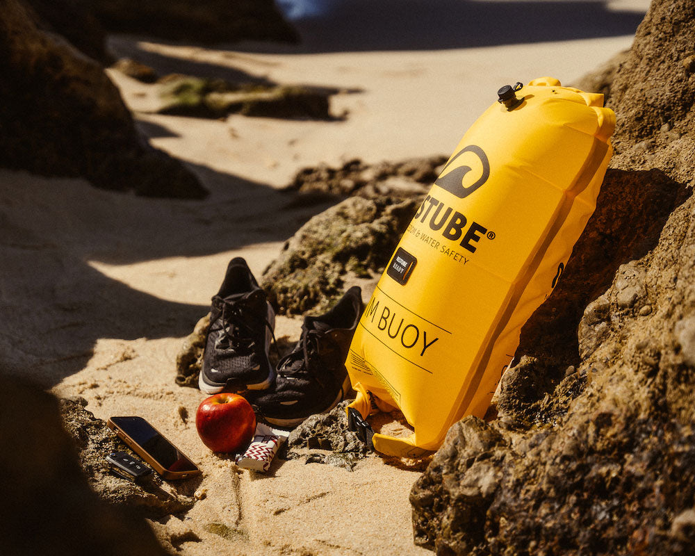 The Swim buoy leaning on the side of a rock on the beach with items from the integrated drybag