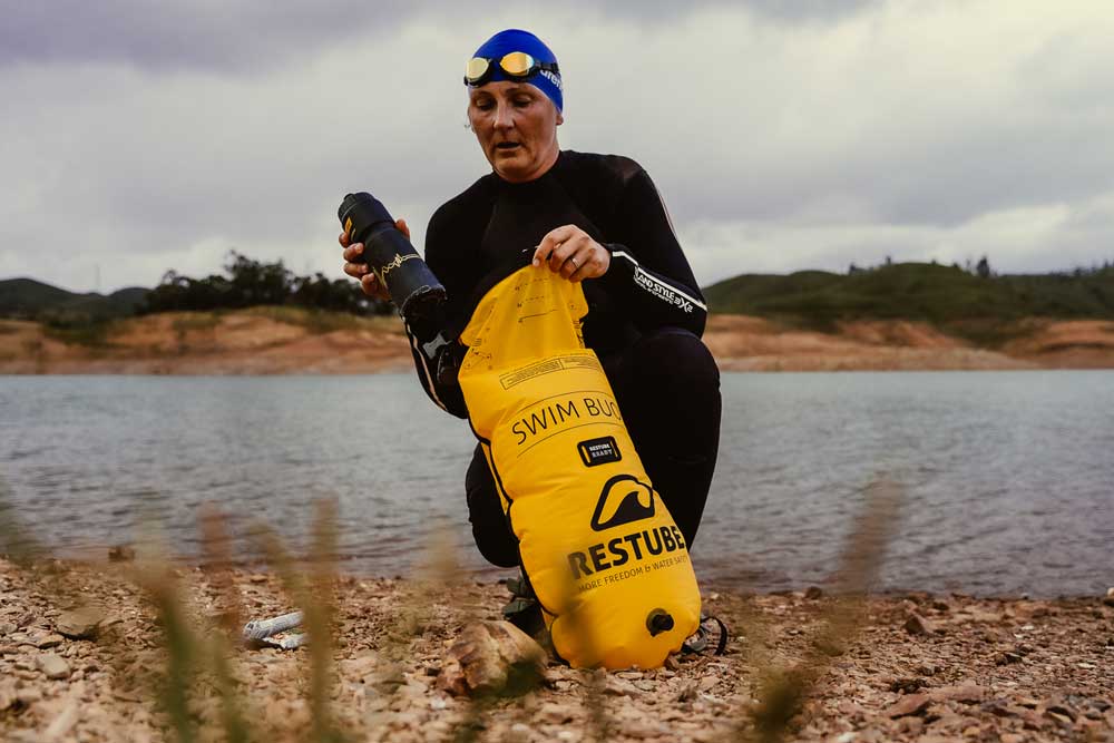 Swimmer packing her posessions in the yellow RESTUBE swim buoy at the lake shore.