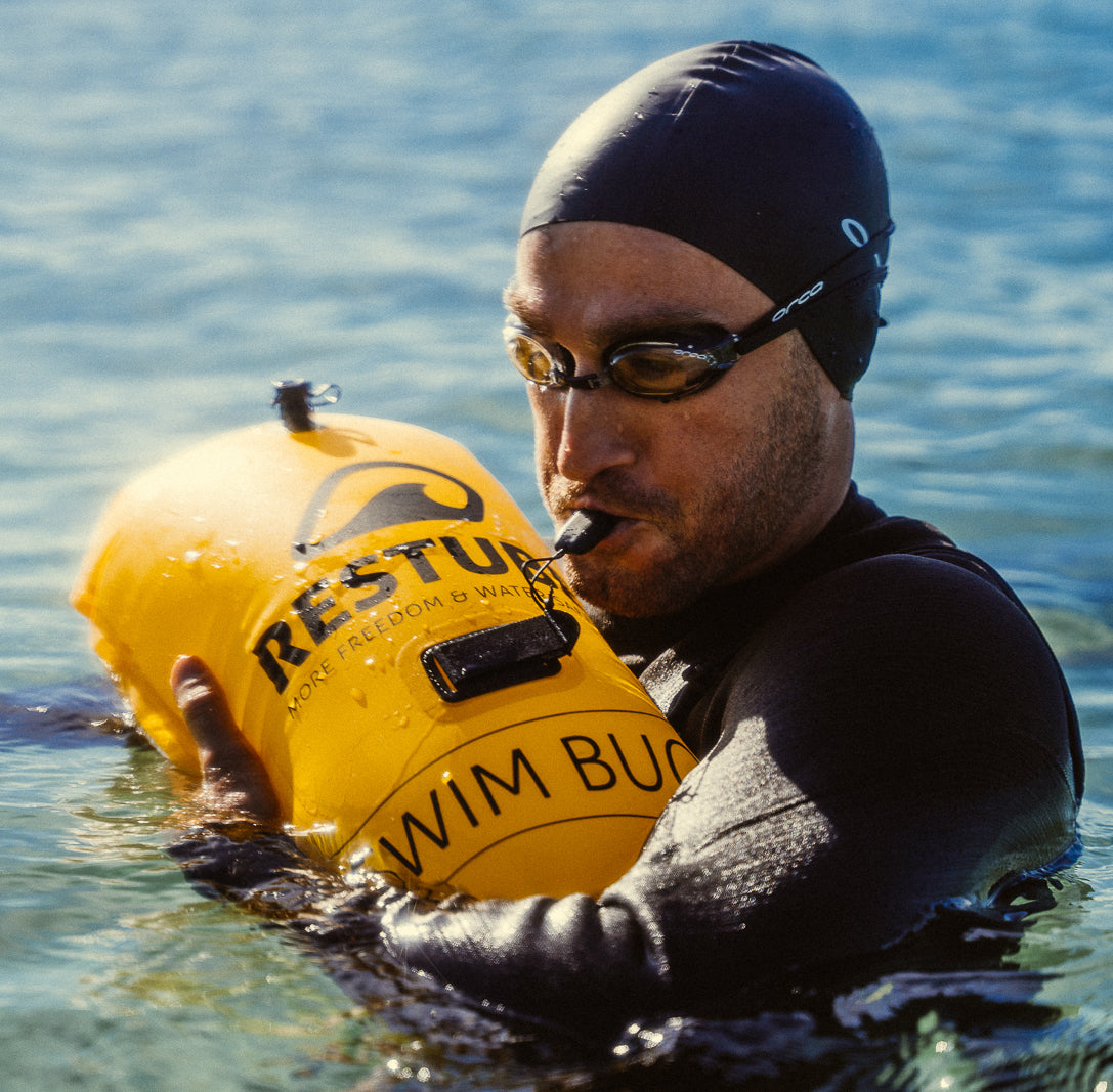 Swimmer blowing the wistle in the yellow RESTUBE swim buoy in the water – for more buoyancy and visibility.