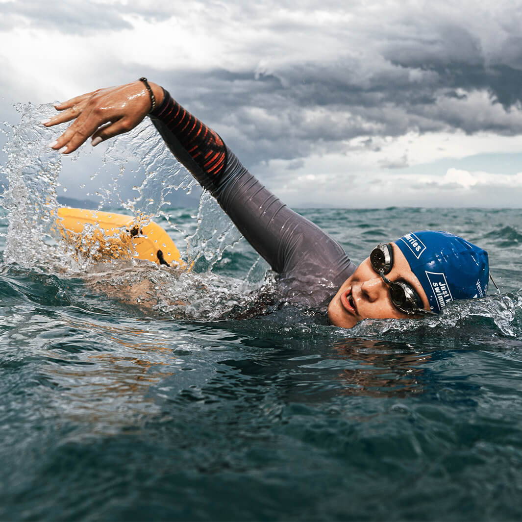 Swimmer in open water with RESTUBE buoy under cloudy sky.