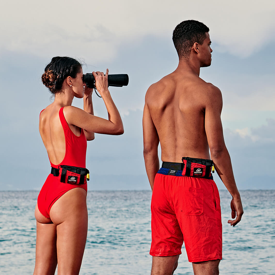 Eine Rettungsschwimmerin mit Fernglas, ein Rettungsschwimmer beide mit einer Restube lifeguard am Meeresstrand.