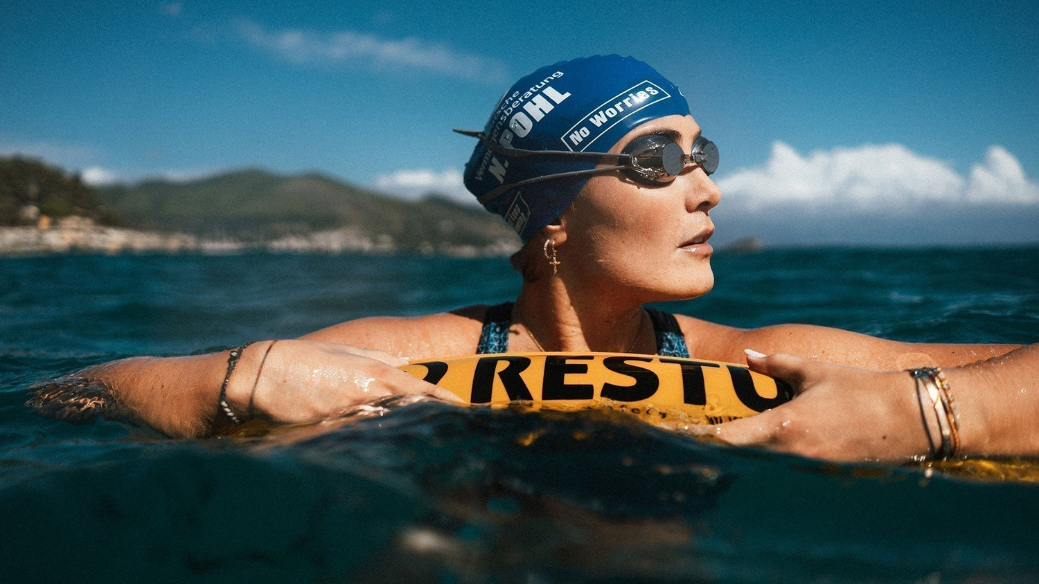 Open water swimmer resting on a yellow RESTUBE safety buoy in the ocean for visibility and flotation