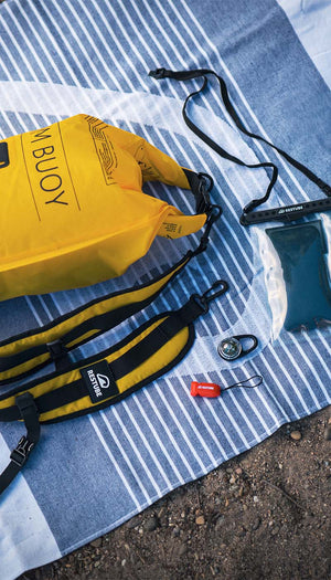 RESTUBE gear laid out on a towel – buoy, whistle, waterproof pouch & strap: safety at hand for your trip.